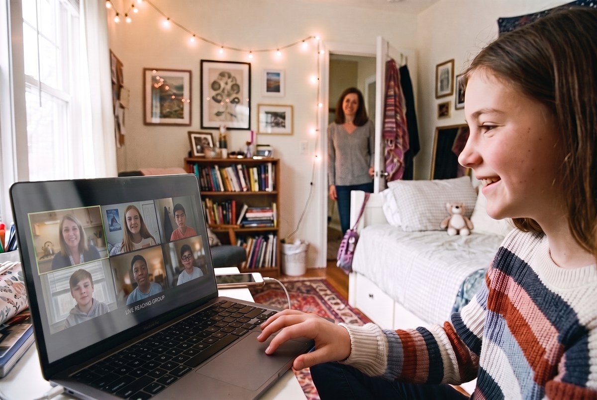 A seventh-grade girl at her bedroom desk in a live online reading group, her teacher and five classmates on screen and her mom in the doorway behind her